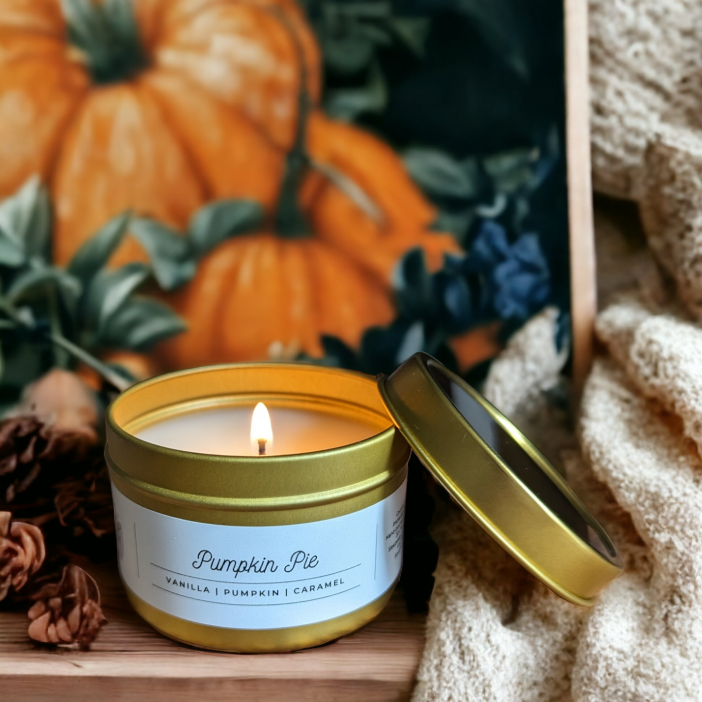A pumpkin pie, scented with vanilla, pumpkin, and caramel. Sits ontop of wood. A painted picture of pumpkins is in the background with pinecones