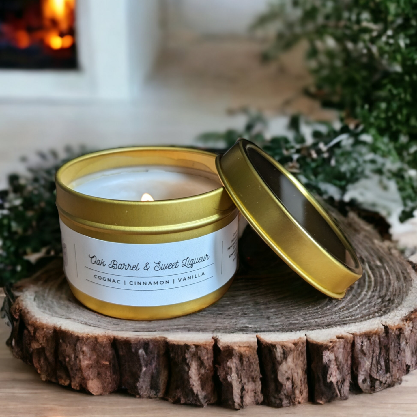 A candle in a 4oz gold tin is displayed on a wooden round with green plant and fireplace in background.