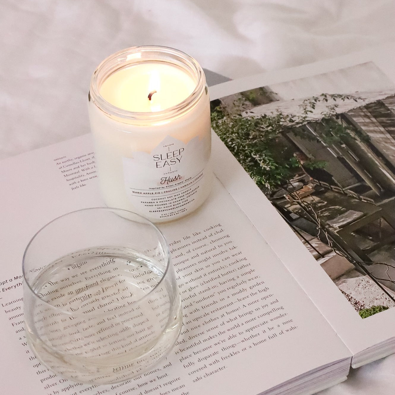Our Hush coconut soy candle is laying on top of a book with wine glass by its side.