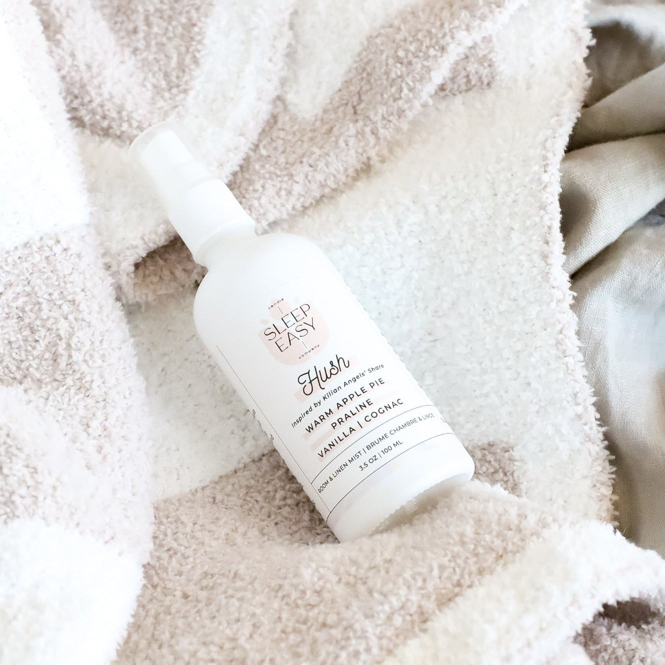 Hush Room & Linen Mist bottle laying on top of a cozy blanket.