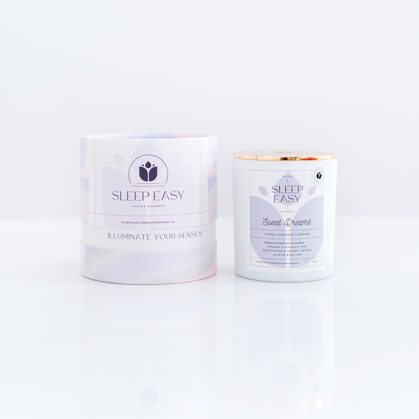 Sweet Dreams coconut soy candle. Citrus, coconut, jasmine flower fragrance.white candle jar with gold lid is displayed on a white background. The label is white and light blue. Logo in the background of the label looks like a delicate flower. Beside the candle jar is a branded tube box with a wavy multi colour texture. Hand poured coconut soy candles. Handmade in Oshawa, Ontario. Luxury candles Canada. Scented candles Canada. Luxury Scented candles. Free Canadian shipping on orders over $99.99.