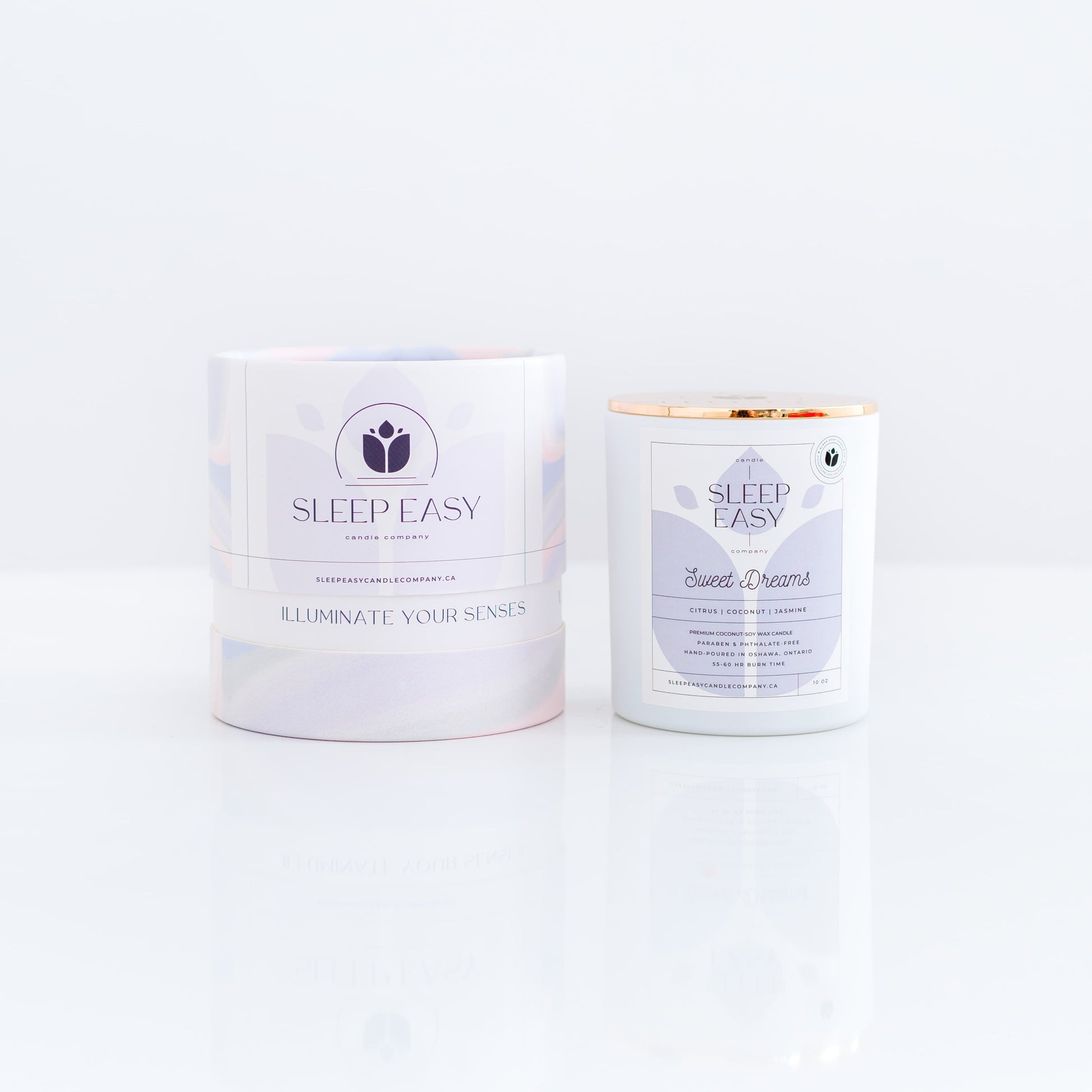 Sweet Dreams coconut soy candle. Citrus, coconut, jasmine flower fragrance.white candle jar with gold lid is displayed on a white background. The label is white and light blue. Logo in the background of the label looks like a delicate flower. Beside the candle jar is a branded tube box with a wavy multi colour texture. Hand poured coconut soy candles. Handmade in Oshawa, Ontario. Luxury candles Canada. Scented candles Canada. Luxury Scented candles. Free Canadian shipping on orders over $99.99.