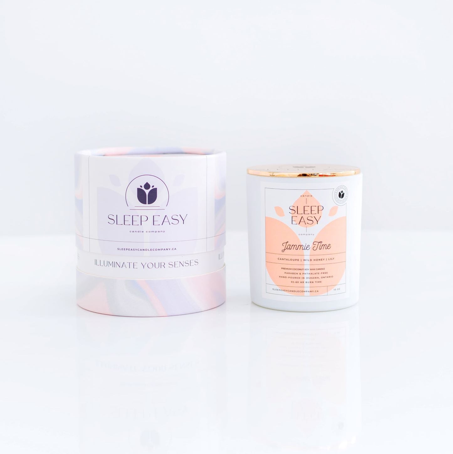 Jammie Time coconut soy candle, white candle jar with gold lid is displayed on a white background. The label is white and light pink. Logo in the background of the label looks like a delicate flower. Beside the candle jar is a branded tube box with a wavy multi colour texture. Hand poured coconut soy candles. Handmade in Oshawa, Ontario. Luxury candles Canada. Scented candles Canada. Luxury Scented candles. Luxury Coconut soy candles. Free Canadian shipping on orders over $99.99.