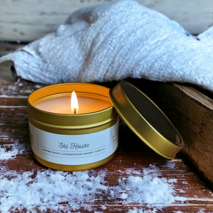 4oz coconut soy candle is displayed on a wooden table with snow in front. A white blanket is displayed in the background. Ski House is inspired by LAFCO SKI House