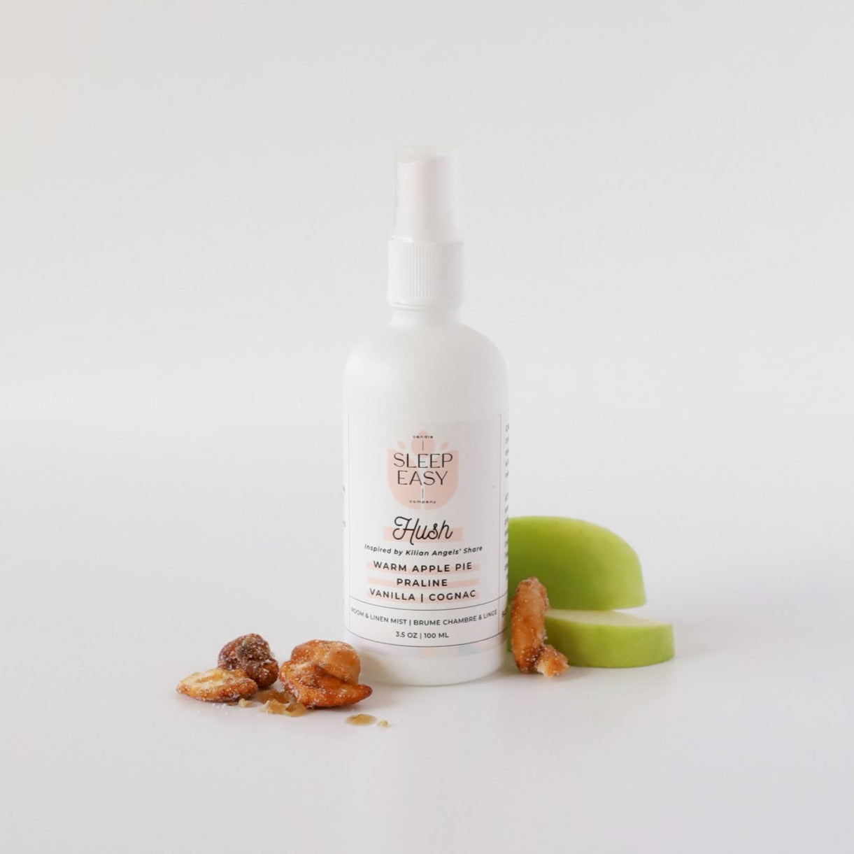 Hush Room & Linen Mist bottle in front of a white background with green apples, and honey praline. 