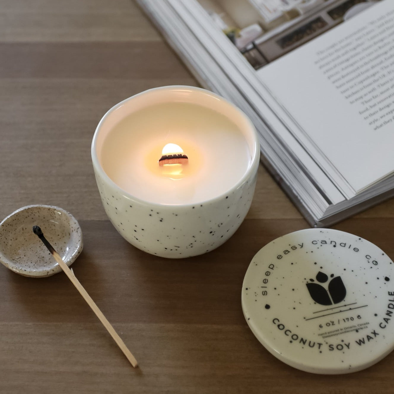 Ceramic Nordic Candle. With Wood Wick on top of a wood table with a book and a match stick. 