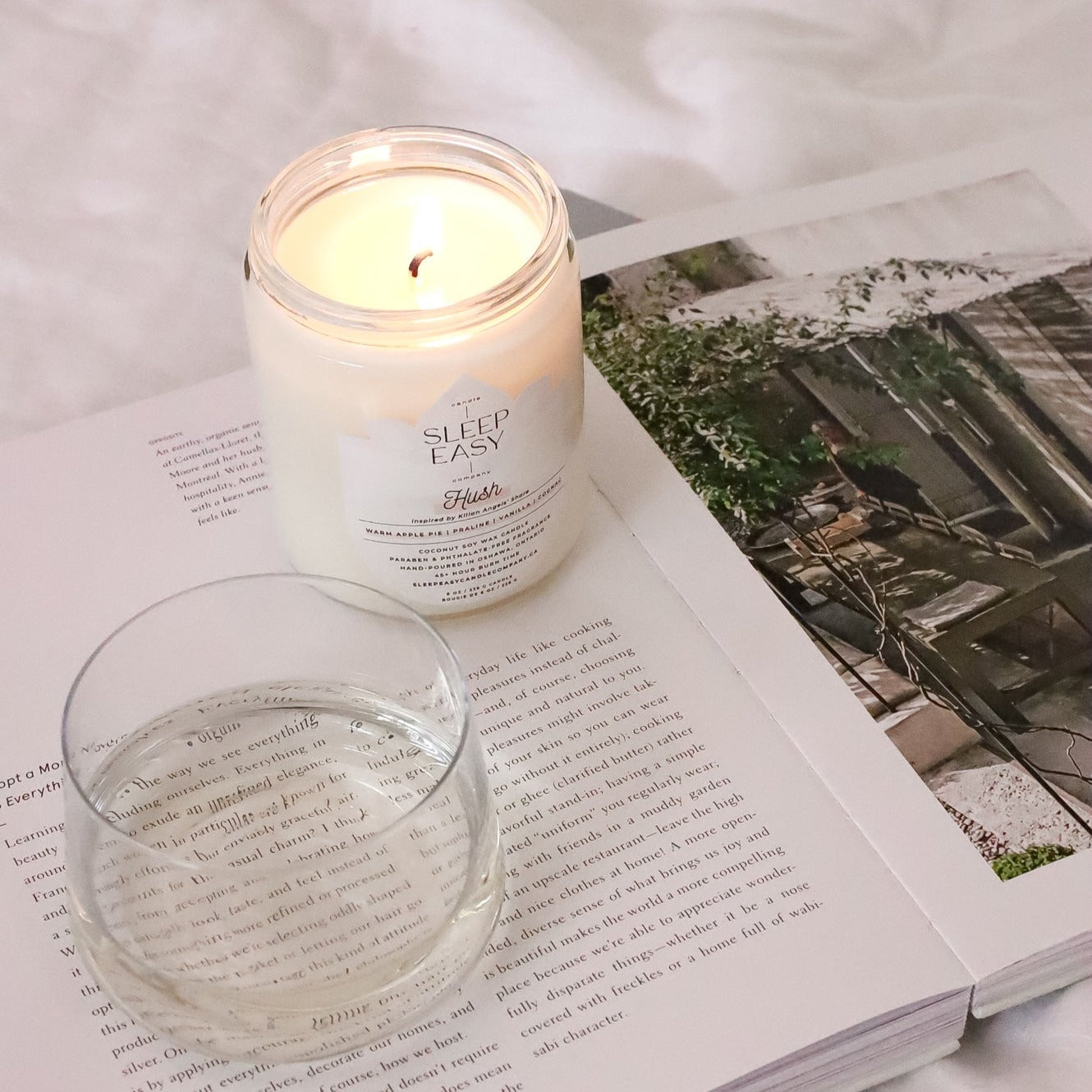 Our Hush coconut soy candle is laying on top of a book with wine glass by its side. 